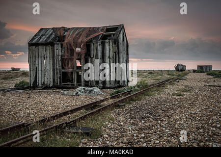 An old abandoned shed on the shingle beach at Dungeness in Kent, just before sunrise the first light of dawn adds a little colour to the sky. Stock Photo