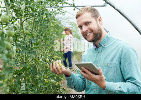 Portrait Of Agricultural Workers Checking Tomato Plants Using Digital Tablet Stock Photo