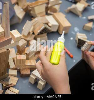Close-up of child's hands playing with wooden constructor, bricks on table. Boy glues blocks to make house, building, square Stock Photo