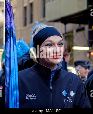 High school girl smiling & holding closed flag in St. Patrick's Day Parade in New York, 2018. Flag captain written  on uniform, sparkles on face. Stock Photo