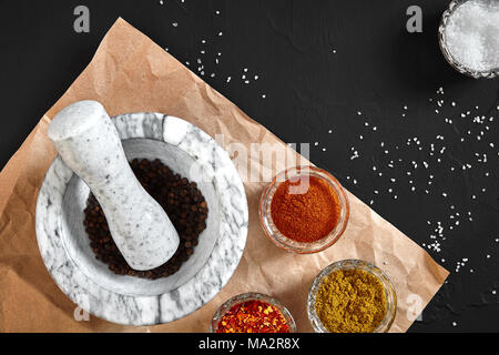 White mortar and pestle with dried peppers in flat lay on black background. Copy space. Still life. Top view Stock Photo