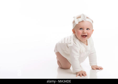 A laughing, crawling, seven month old, baby girl wearing a white shirt, diaper and headband. Shot in the studio on a white, seamless backdrop. Stock Photo