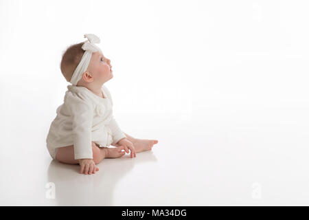 A profile view of a smiling, seven month old, baby girl wearing white. Shot in the studio on a white, seamless backdrop. Stock Photo