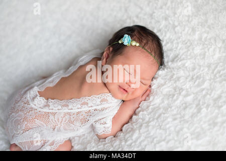 Portrait of a seven day old, smiling, sleeping, newborn baby girl wearing a white, lace romper. Stock Photo