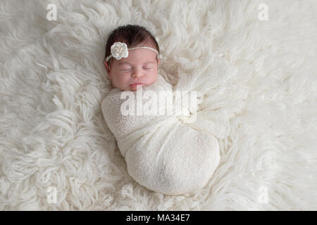 Sleeping, ten day old newborn baby girl swaddled in a white wrap. Shot in the studio on a white sheepskin rug. Stock Photo