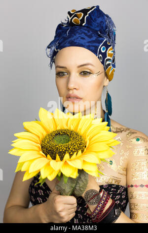 Model woman in African style clothes with a sunflower in hands on a photo session Stock Photo