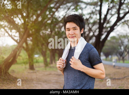 young sporty man with white towel resting after workout sport exercises outdoors at the park Stock Photo