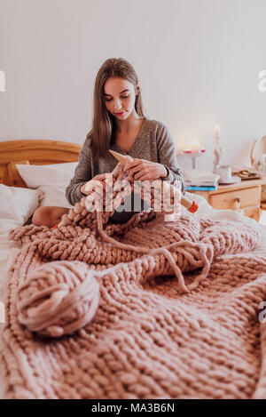 young woman sitting in bed and knitting with XXL wool Stock Photo