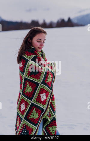 young woman wrapped in a blanket is standing in the snow, Stock Photo