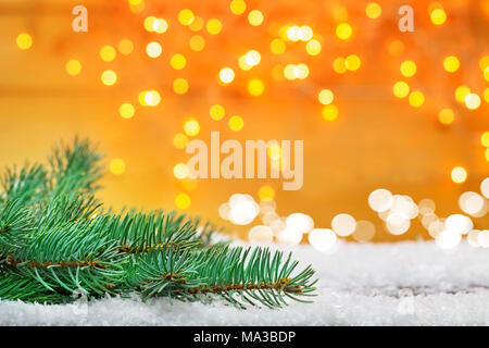 Christmas background, fir branch in the snow in front of bokeh, golden lights Stock Photo