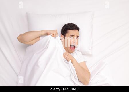 Terrified young man lying in bed and screaming Stock Photo