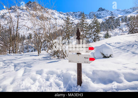 Sign buried in deep snow showing directions and walking times near Morskie Oko lake in winter season, Tatra Mountains Stock Photo
