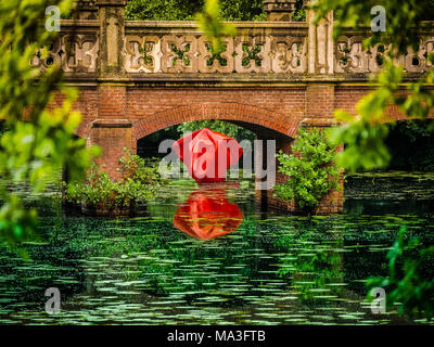 Red artwork below bridge on lake with water lilies at Moyland Castle in Bedburg-Hau, Germany Stock Photo