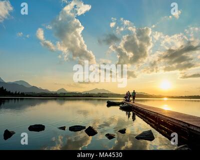 The sun setting over the Hopfensee lake in the Allgäu region of Bavarian Swabia, Bavaria, Germany Stock Photo