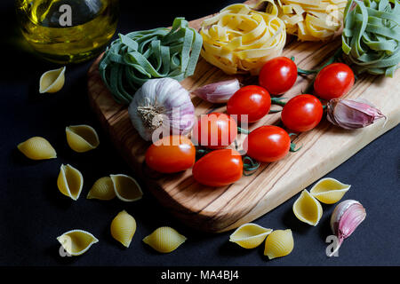 Close up Chiaroscuro Dark Food Pasta ingredients with spaghetti,  tagliatelle and penne tricolore and garlic with olive oil with copy space Stock Photo