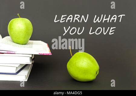 Two green apples and open books on gray background with words learn what you love. Concept back to school Stock Photo