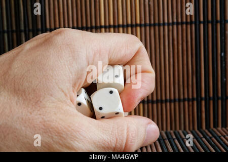 Stack of three white plastic dices in man's hand on brown wooden table background. Six sides cube with black dots. Stock Photo