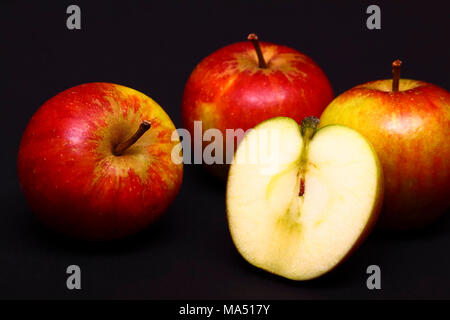 Three red whole apples and one sliced in half isolated on a black background Stock Photo