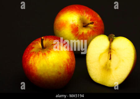 Two whole red apples and one sliced in half isolated on a black background Stock Photo