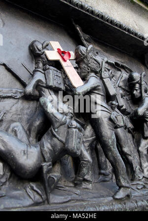 GLASGOW, SCOTLAND -JANUARY 8TH 2015: A carved soldier from a war memorial. Is holding a small wooden cross with a red poppy on it. Stock Photo