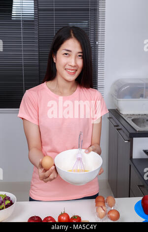 woman cooking and whisking eggs in a bowl in kitchen room Stock Photo