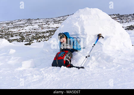 hiker pours himself a tea from a thermos, sitting in a snowy house igloo against a background of a winter mountain landscape Stock Photo