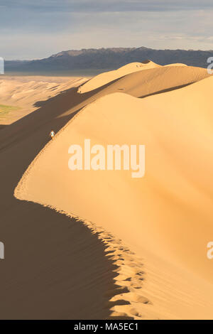 Woman walking on Khongor sand dunes in Gobi Gurvan Saikhan National Park. Sevrei district, South Gobi province, Mongolia. Stock Photo