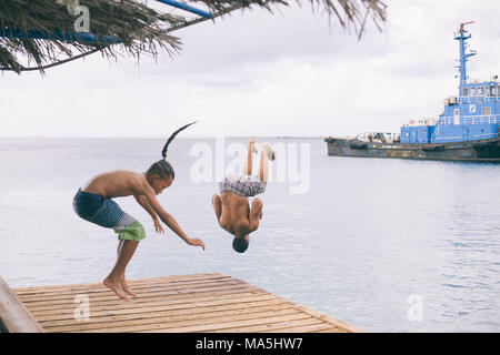 two guys jumping on a dock to the water Stock Photo