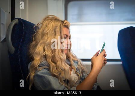 Female passenger in casual clothes sits alone inside the train and ready to departure. Young serious woman looking in smartphone and have fun in trip Stock Photo