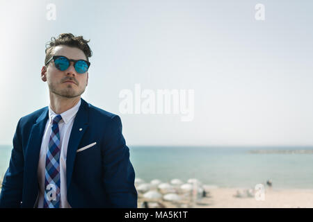 Young serious man in elegant suit and sunglass on background of sea and sky. Successful manager is relaxing outdoors in sunny day. Trendy guy Stock Photo