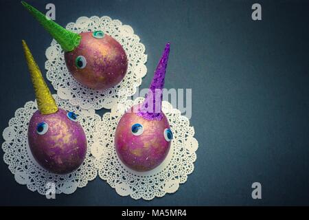Easter cosmic purple and gold painted eggs unicorns with eyes and colorful sparkling horns on black background with lace napkins. Copyspace. Top view Stock Photo