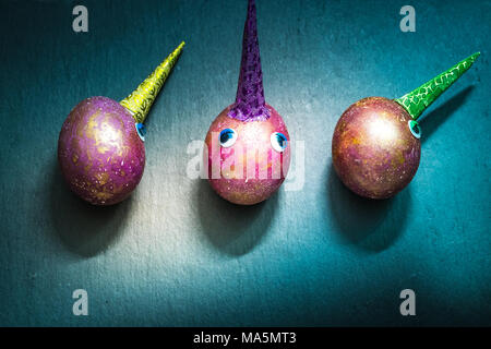 Three funny unicorn easter space colored purple marble eggs with horns and eyes on slate cutting board. Top view.hap Stock Photo