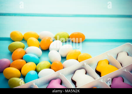 Scattered easter colorful sweet chocolate small eggs with candy bunnies on pastel blue wooden background. Copyspace Stock Photo