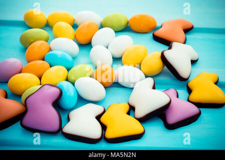 Scattered easter colorful sweet chocolate small eggs with candy rabbits on pastel turquoise wooden background. Copyspace Stock Photo