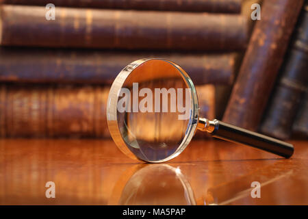 Still life with magnifying glass standing on wooden table on background with old books Stock Photo