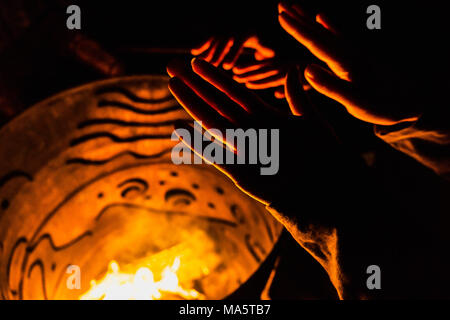 Close-up view of people warming up their hands over a fire burning in an iron barrel on a cold night. Stock Photo