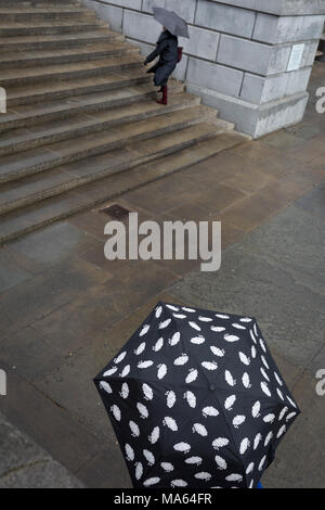 Two people carrying umbrellas in Trafalgar Square, on 29th March, 2018 in London, England. Stock Photo