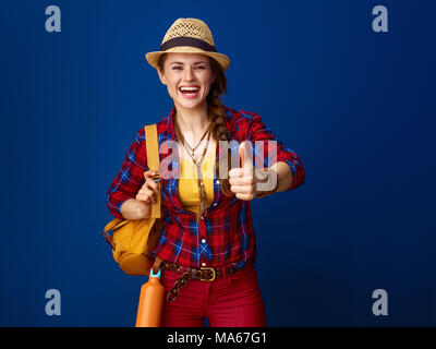 Searching for inspiring places. smiling young traveller woman with backpack showing thumbs up on blue background Stock Photo