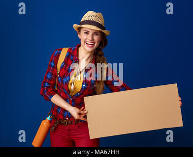 Searching for inspiring places. happy young traveller woman with backpack showing blank board against blue background Stock Photo