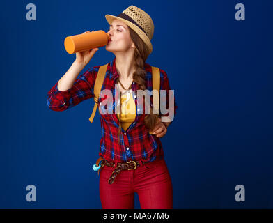 Searching for inspiring places. young traveller woman in a plaid shirt drinking water from bottle on blue background Stock Photo