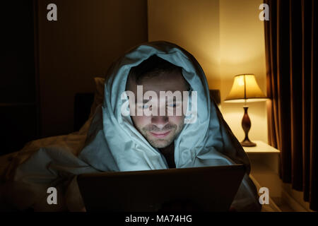 Handsome young man at home reading with tablet PC lying on bed at night. He is tired and want to sleep Stock Photo