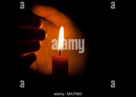 A burning candle at night, protected by the hand of a woman. Candle flame glowing on a dark background with free space for text. Close up, shallow dep Stock Photo