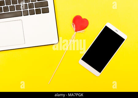 symbol heart of a smartphone laptop. A decorative heart on a yellow background together with smart gadgets. Stock Photo