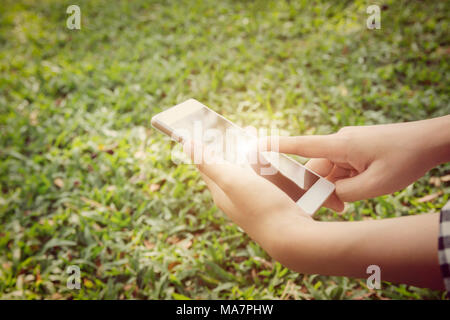 Closeup of young woman hands using a smartphone. Nature background. Stock Photo