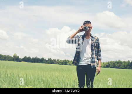 Young hipster handsome man photography standing shooting retro camera with nature enjoy and happy at grassland. Stock Photo
