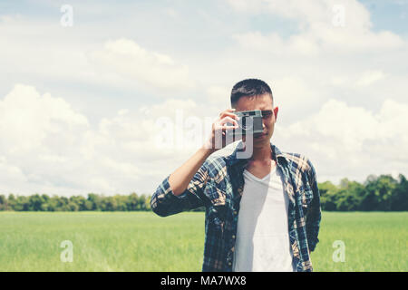 Young hipster handsome man photography standing shooting retro camera with nature enjoy and happy at grassland. Stock Photo