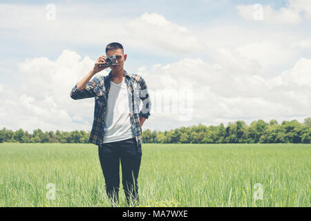 Young hipster handsome man photography standing shooting retro camera with nature enjoy and happy at grassland. Stock Photo