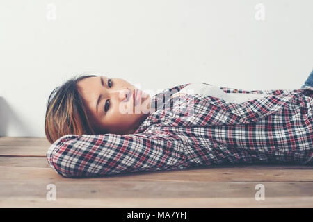 Lonely sad woman deep in thoughts lay down on wooden floor. Stock Photo