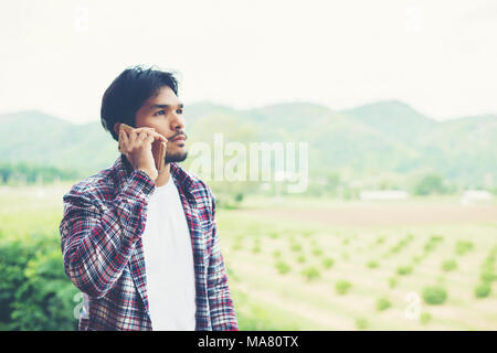 Young hipster bearded man talking on phone, smiling, outside mountain view. Stock Photo