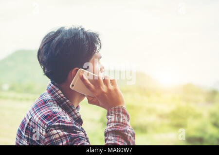 Young hipster bearded man talking on phone, smiling, outside mountain view. Stock Photo